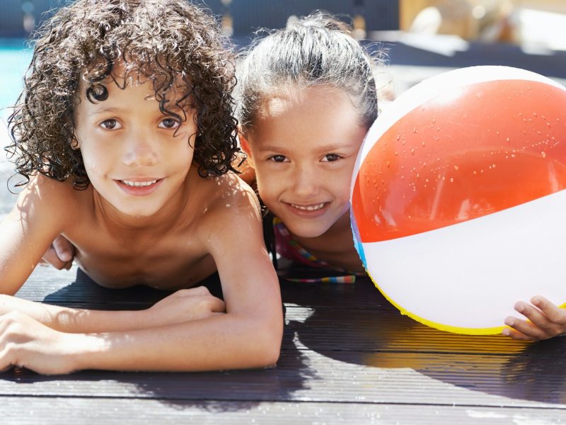 Enjoying the sun and a swim. Portrait of two children lying by a swimming pool on a sunny day.