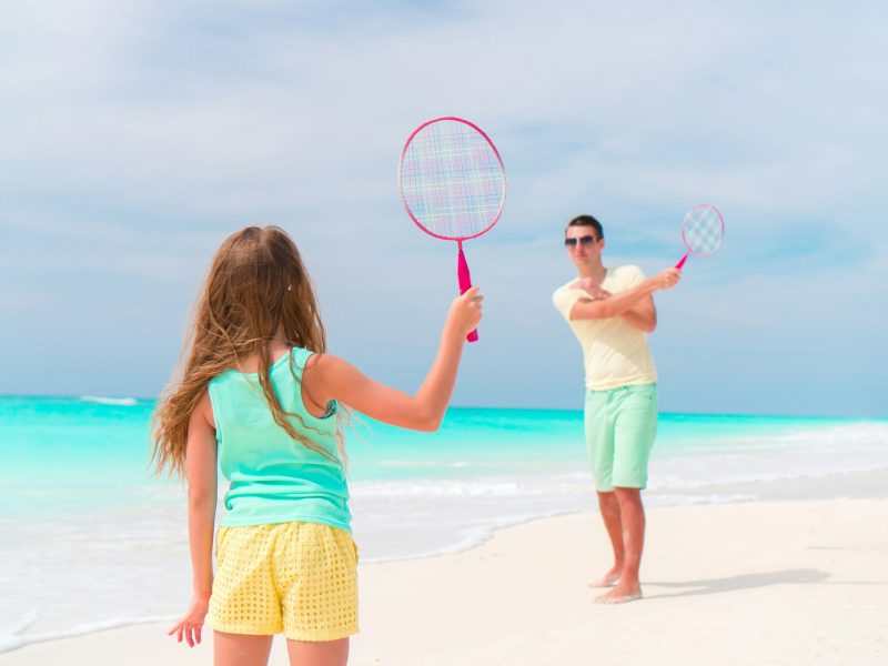 Little girl playing beach tennis on vacation with dad